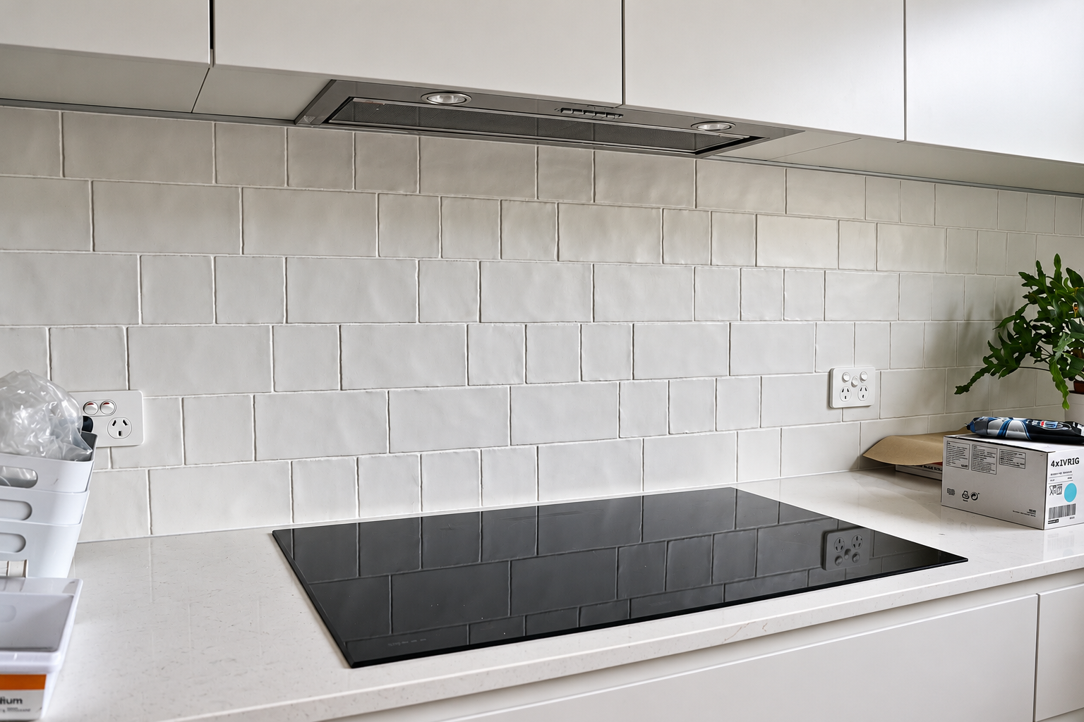 Kitchen cooktop with a light tiled splashback, white cabinetry and pale benchtop