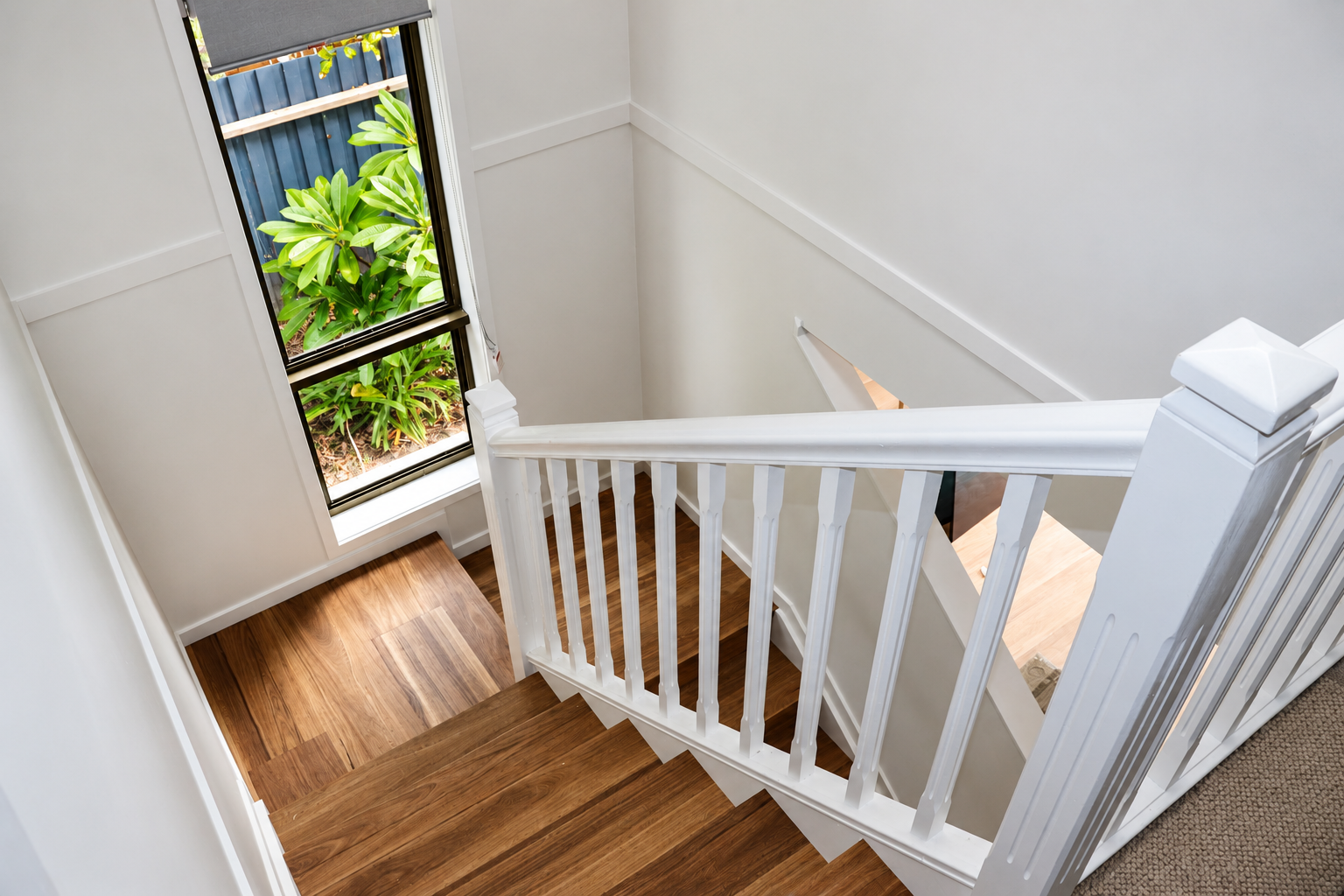 White-painted staircase with turned balusters and spotted gum treads beside a garden window