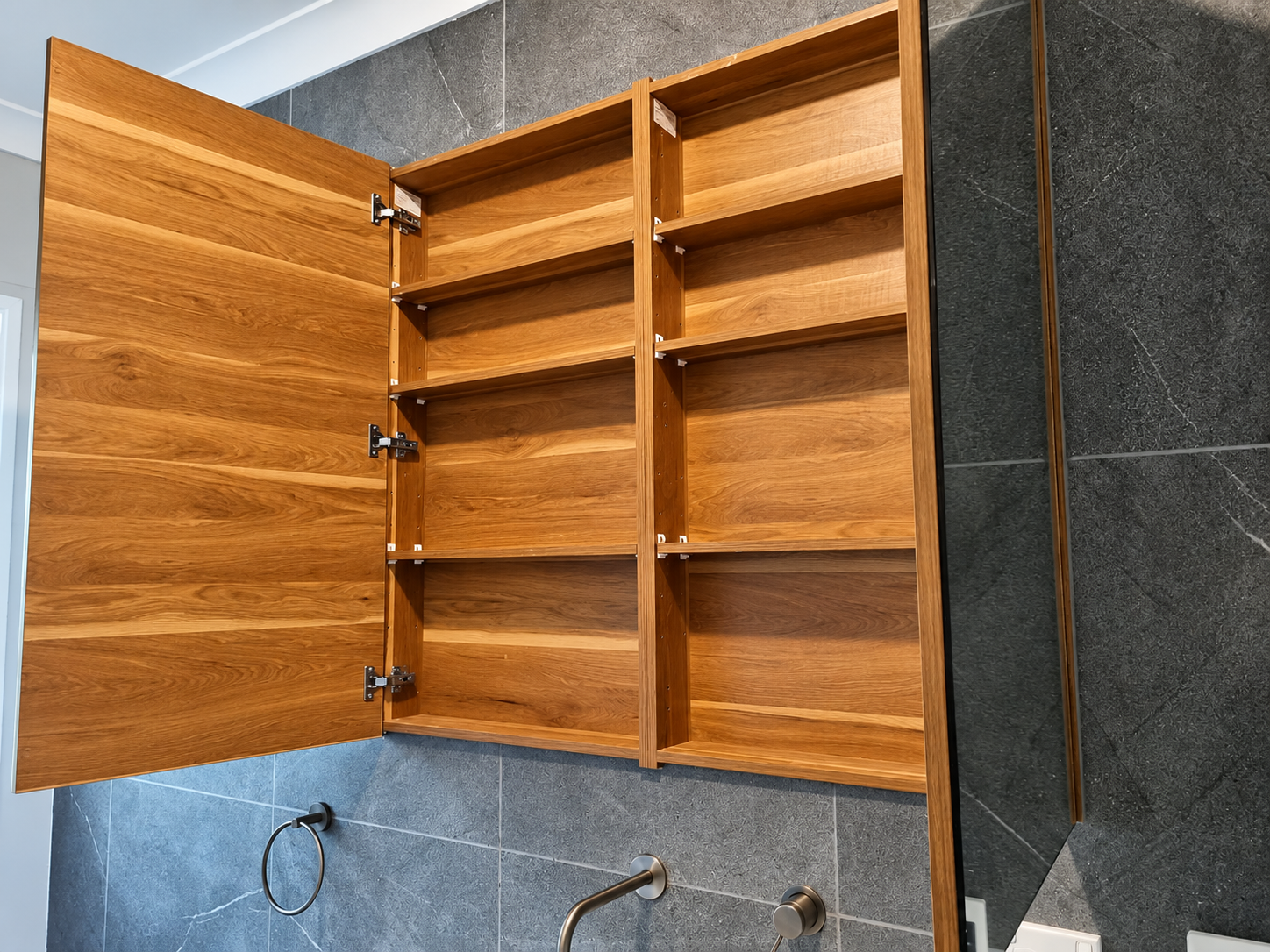 Open timber bathroom cabinet with adjustable shelves against dark tiled walls